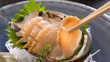 A bowl of sashimi with chopsticks, garnished with green leaves and a small sprig of herb.