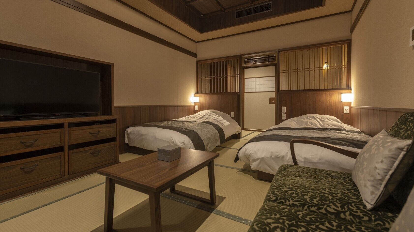 Una habitación de hotel con dos camas, televisión, muebles de madera e iluminación en la pared.