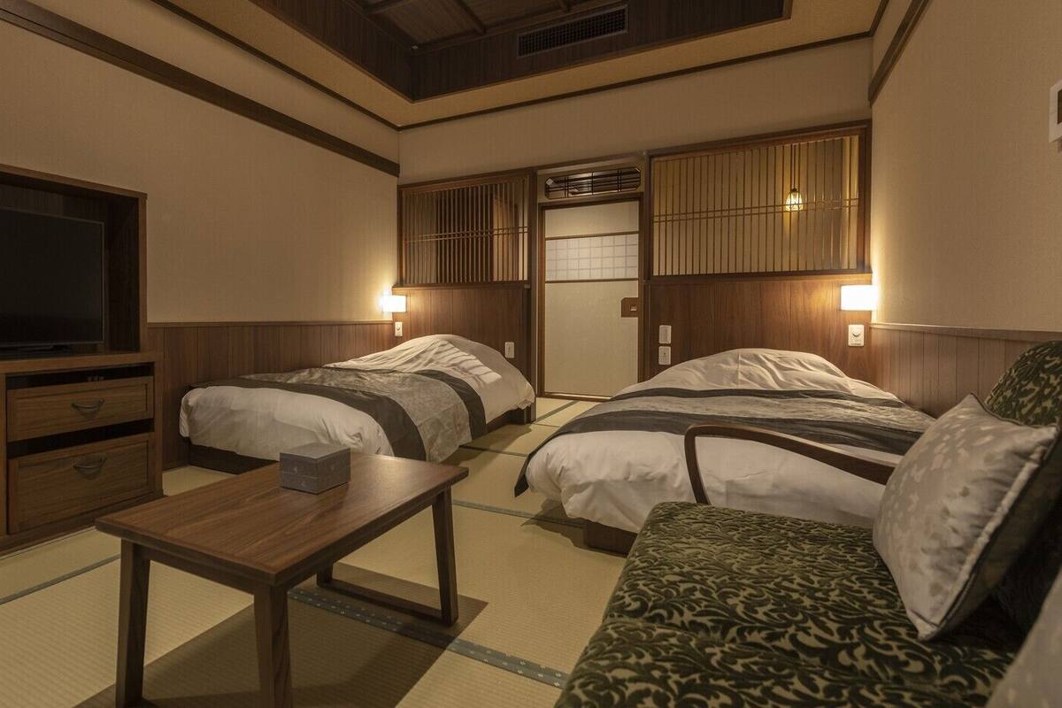 Ein Hotelzimmer mit zwei Betten, einem Fernseher, Holzmöbeln und Wandleuchten.