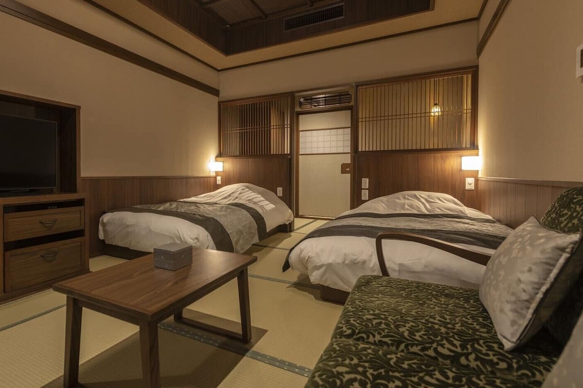 Una habitación de hotel con dos camas, televisión, muebles de madera e iluminación en la pared.