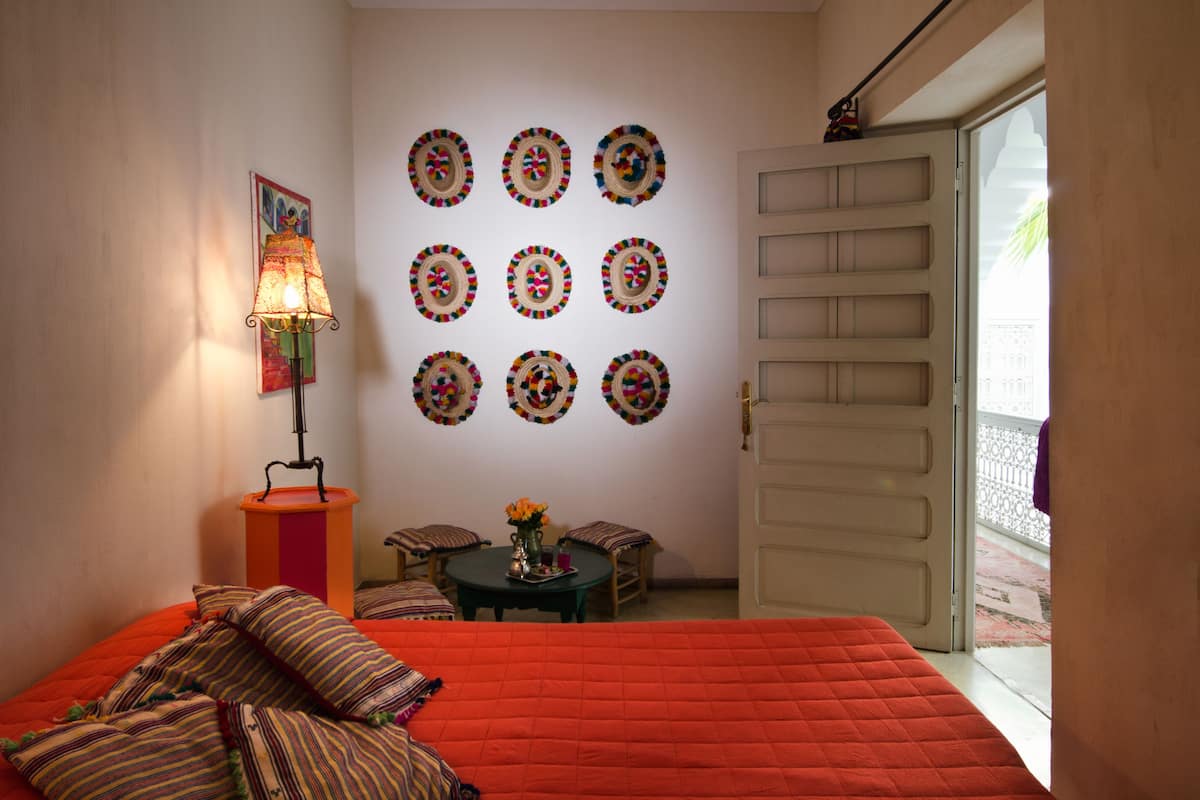 Quarto com uma cama grande, mesa de cabeceira com luminária, mesa redonda com cadeiras e parede decorada com padrões circulares.