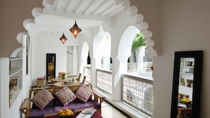 A cozy living room with a sofa, a dining table, and a balcony with white arches and a railing. - Riad Vert Marrakech (Marrakech)