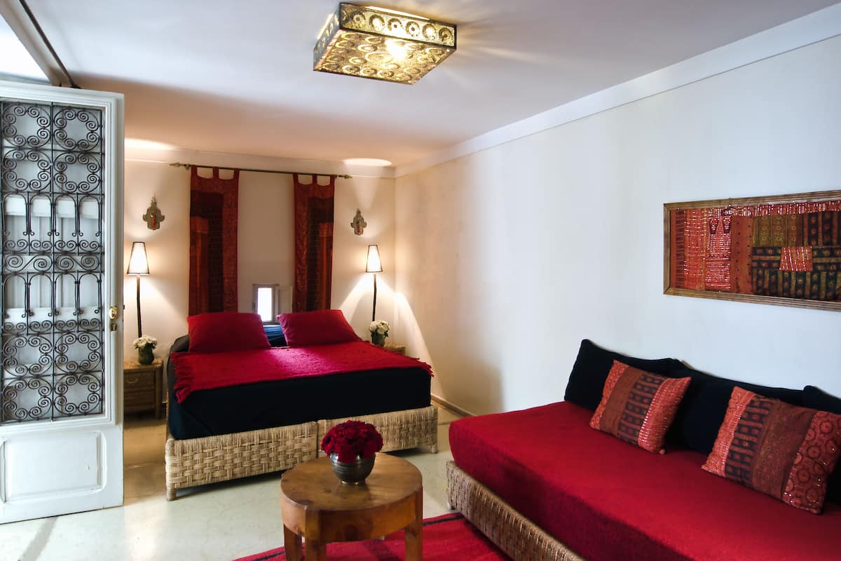 Quarto com duas camas, um sofá, uma mesinha com um vaso e um objeto decorativo na parede.