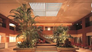 A spacious indoor area with a central staircase, surrounded by red chairs and tables, and large potted plants.