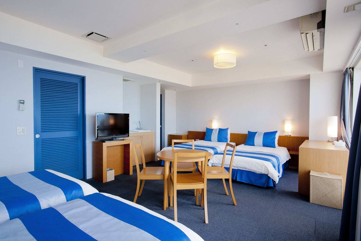 A hotel room with two beds, a desk with a TV, a dining table with chairs, and a small seating area.