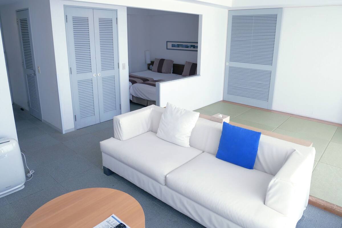 A modern hotel room with a white sofa, a small round table, and a bed with a window.