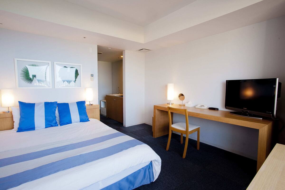 A hotel room with a bed, a desk with a chair, a television, and artwork on the wall.