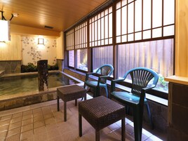 Una habitación tradicional japonesa con suelo de tatami, un pequeño onsen interior y vistas a través de paneles shoji.