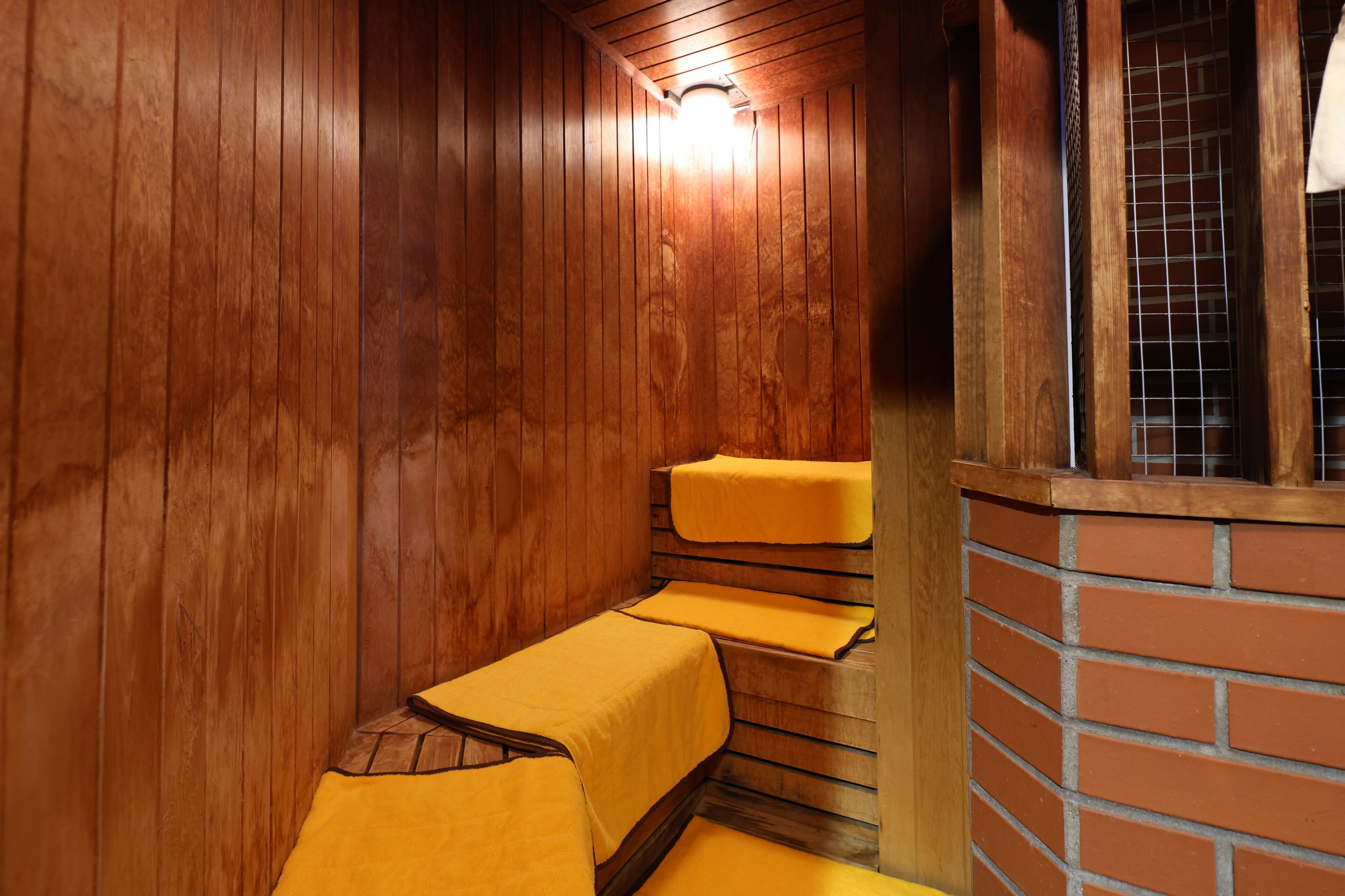 Un interno in legno con un muro in mattoni e una finestra. Si vedono tre tavoli rivestiti di giallo e una panca.