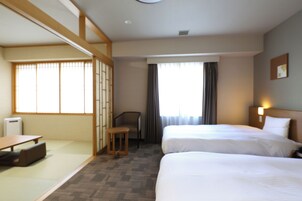 Habitación de hotel con dos camas, una mesita, una silla y un sofá cama.
