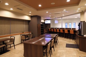 Una sala de conferencias con una larga mesa, sillas, una pantalla de televisión y una pantalla de proyección.