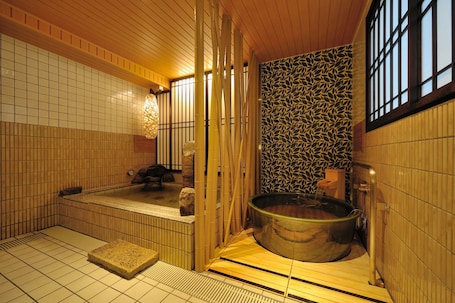 A traditional Japanese onsen with a stone hot spring, wooden flooring, and tiled walls.