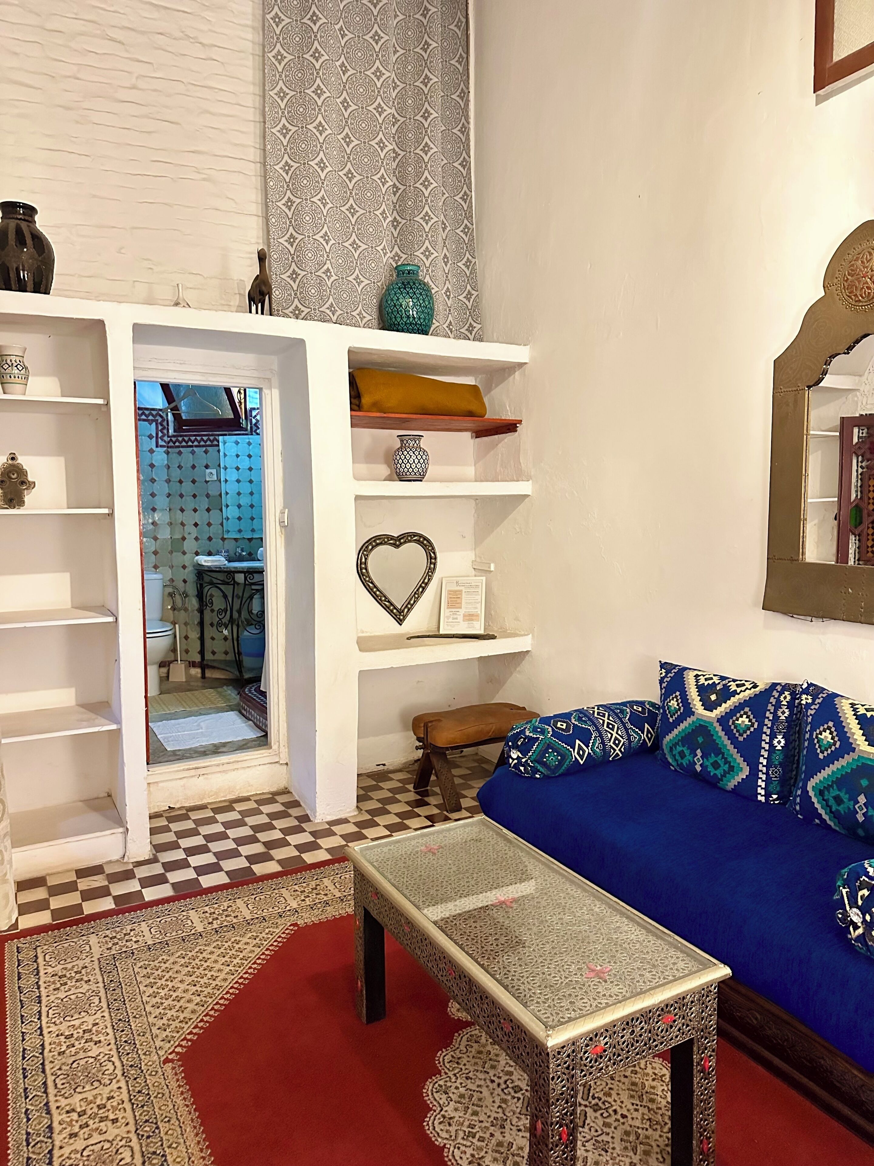 Een woonkamer met een zwart-wit schachbordvloer, een blauwe bank met gestreepte kussens, een bijzettafeltje en planken met decoratieve objecten.