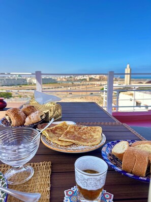 A table with pastries, bread, a glass of tea, and a view of a bridge and landscape. - Riad à la Belle Etoile (Salé)