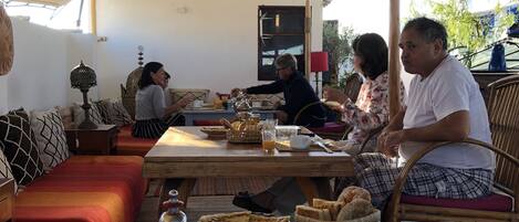 A dining area with a table set for breakfast, including bread, fruit, and tea.