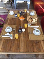 Una mesa de madera dispuesta para el desayuno, con zumo de naranja, yogur y bollería.