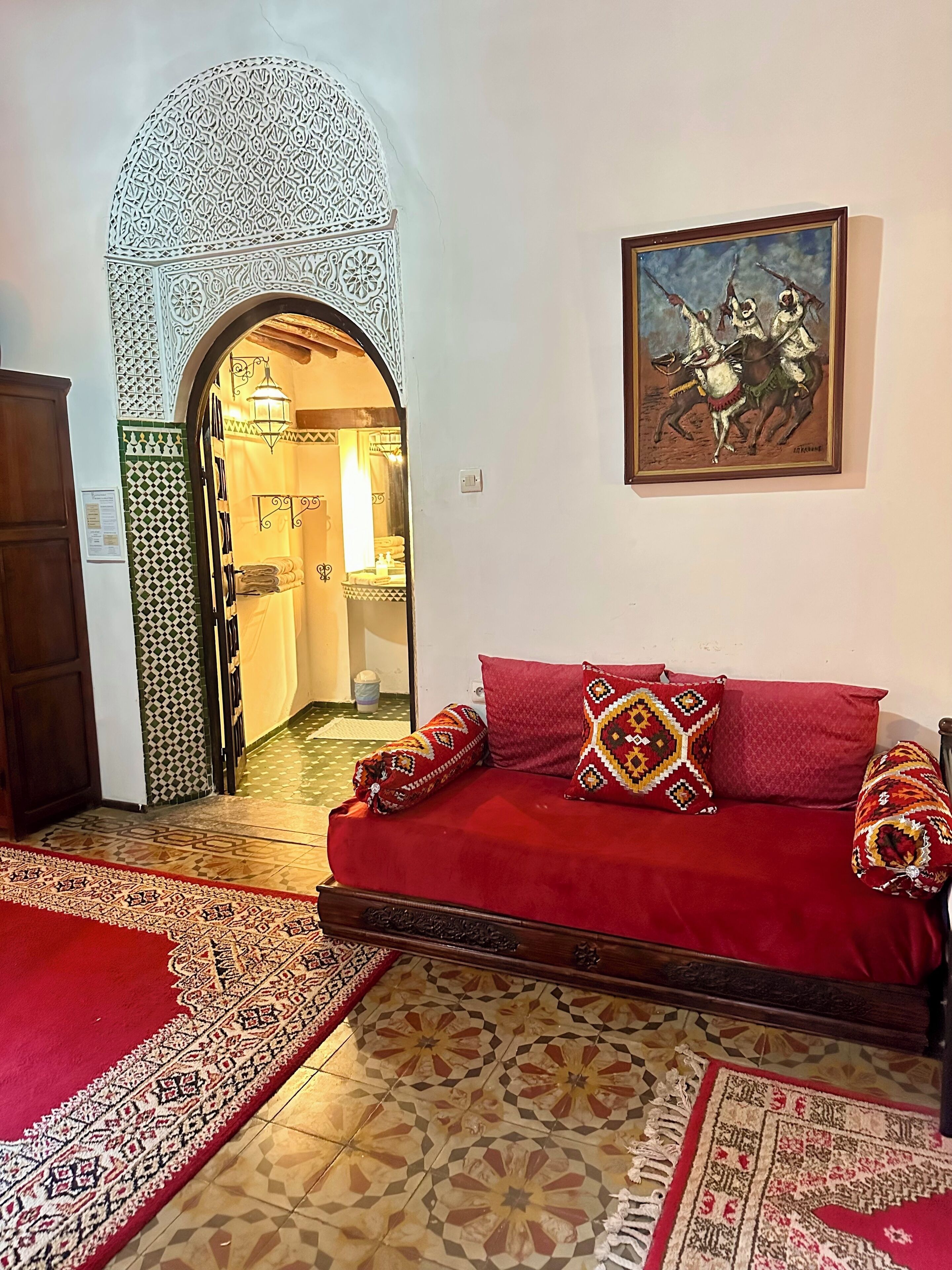 Una habitación con un sofá rojo, alfombras estampadas, un arco decorativo y un cuadro en la pared.