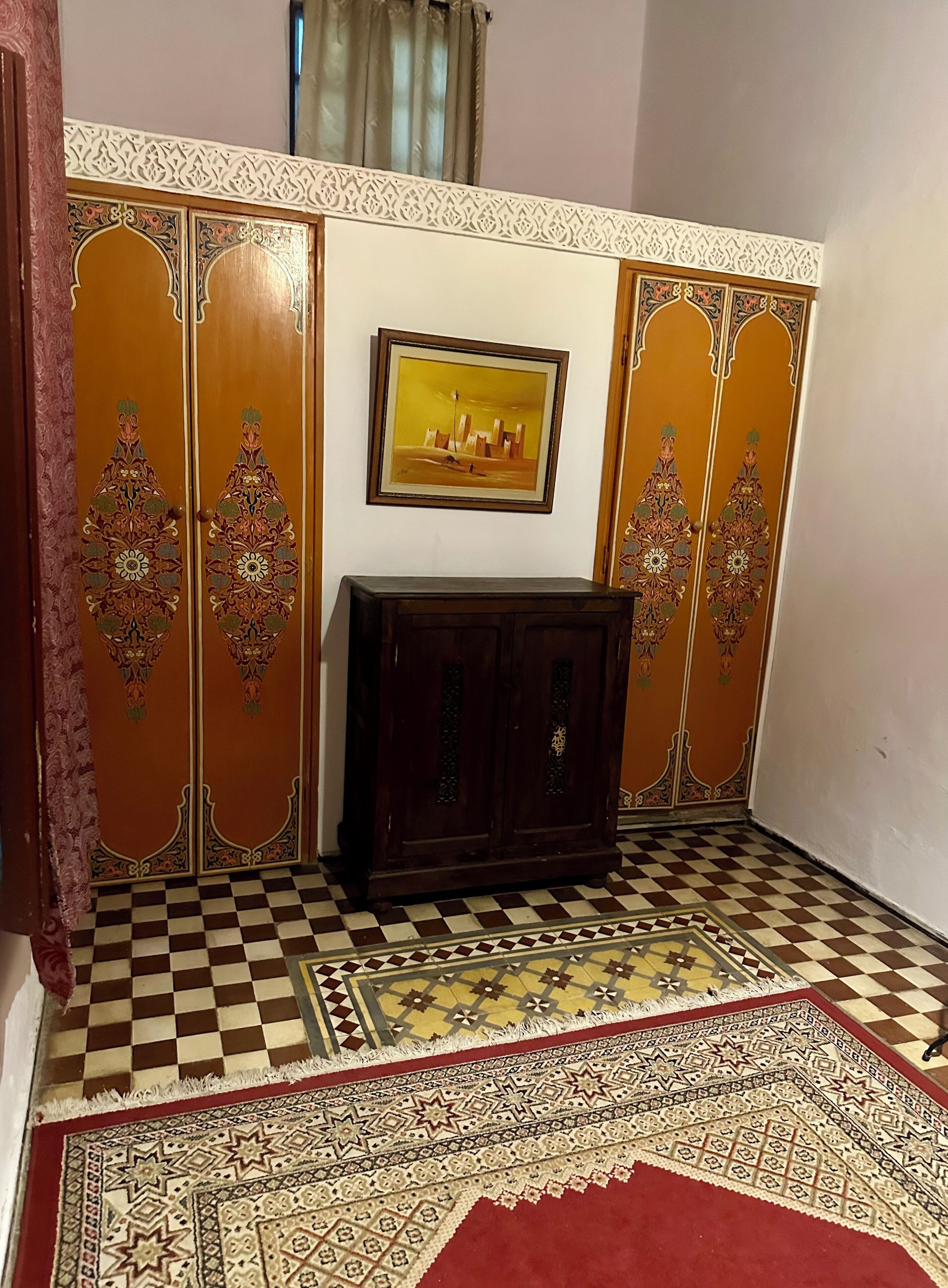 A room with a checkered floor, a patterned rug, a wooden cabinet, and a wall with decorative panels.