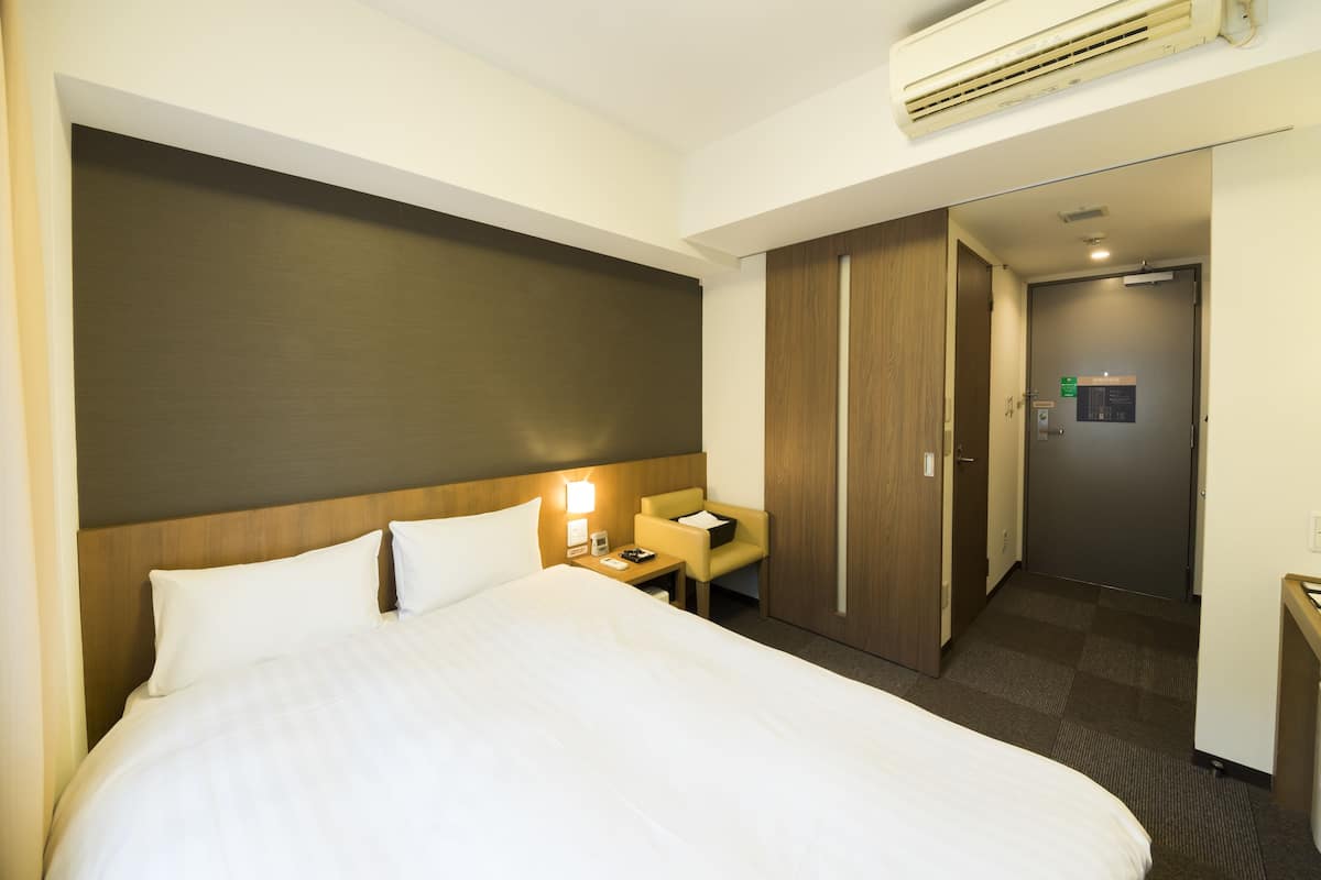 A hotel room with a large bed, a nightstand, a desk, and a wardrobe.