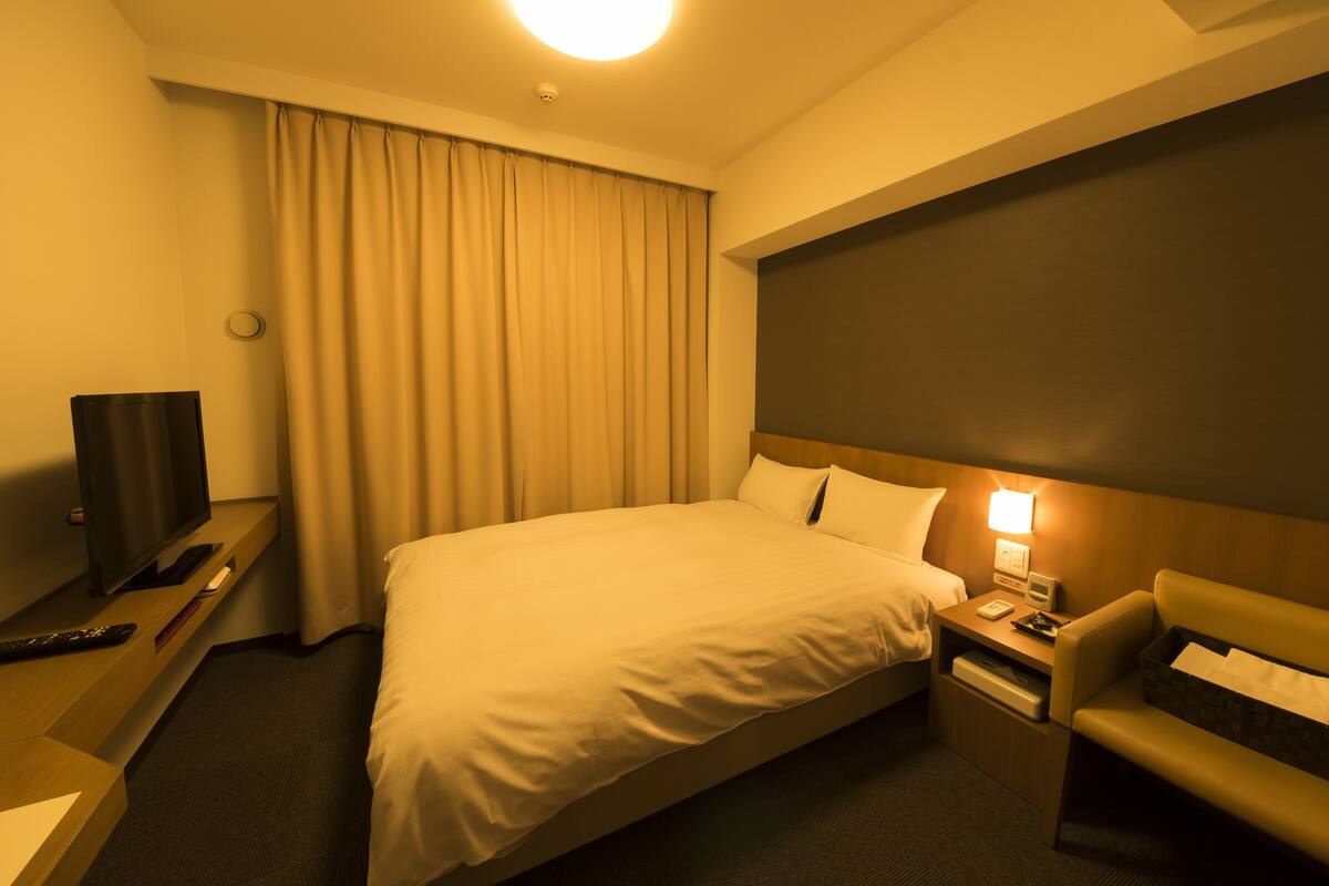 A hotel room with a large bed, a bedside table with a lamp, a TV, and a chair.