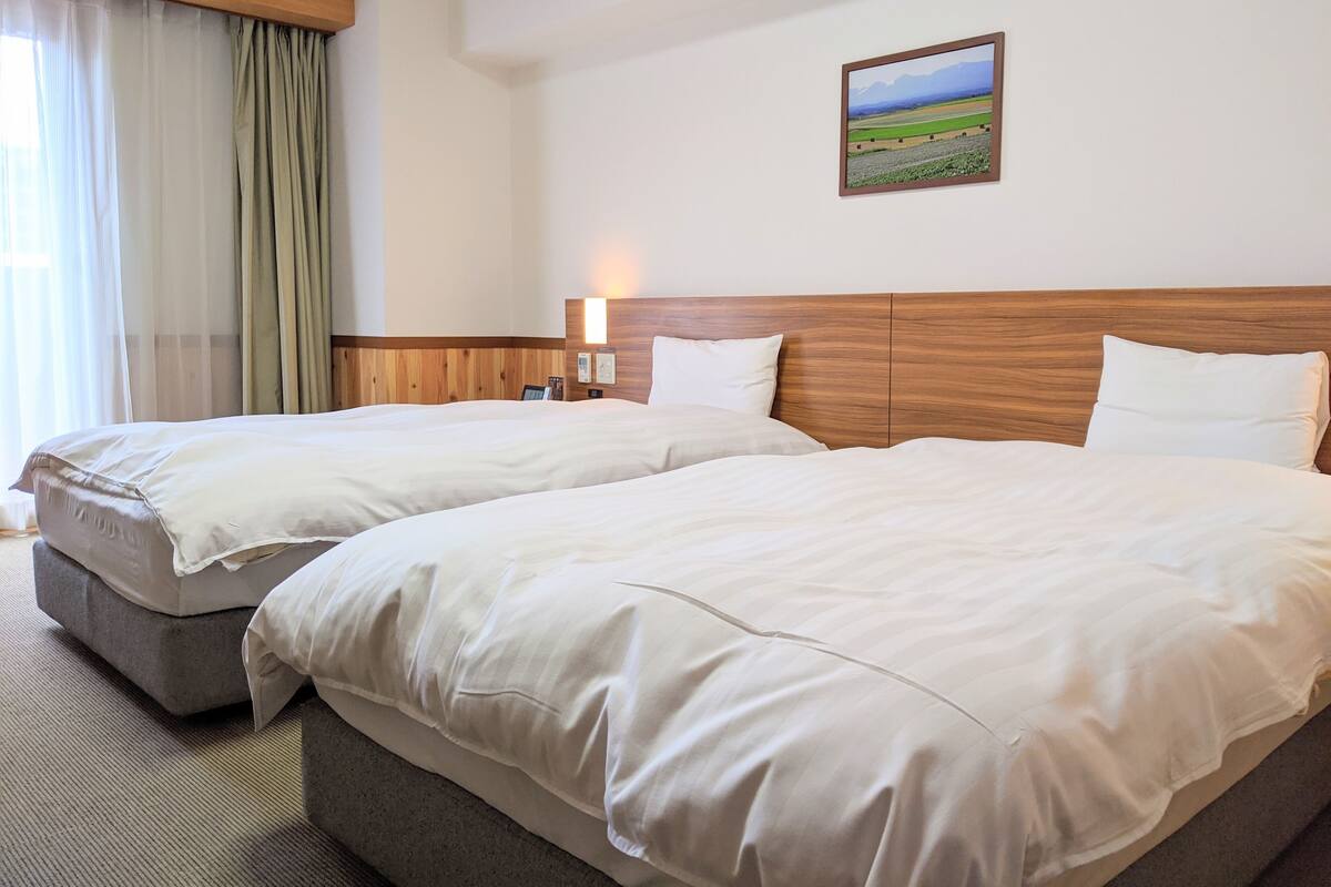 A hotel room with two beds, a wooden headboard, a nightstand with a lamp, and a framed picture on the wall.