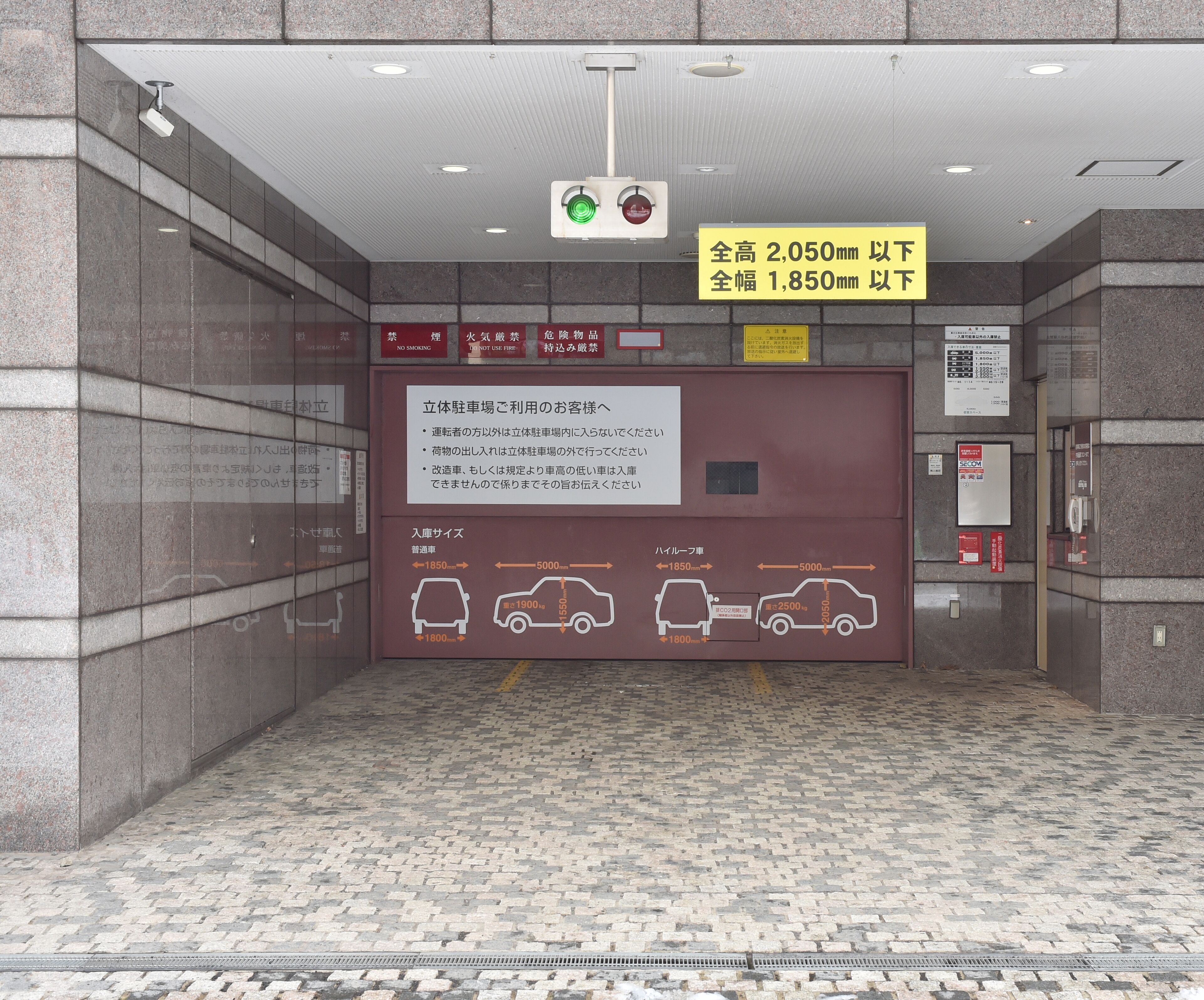 A parking garage entrance with height and width restrictions, a sign with instructions, and a floor with a brick pattern.