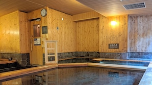 A wooden interior with a stone-lined pool, wooden benches, a clock, and a sign. - Dormy Inn PREMIUM Sapporo Hot Spring (Sapporo)