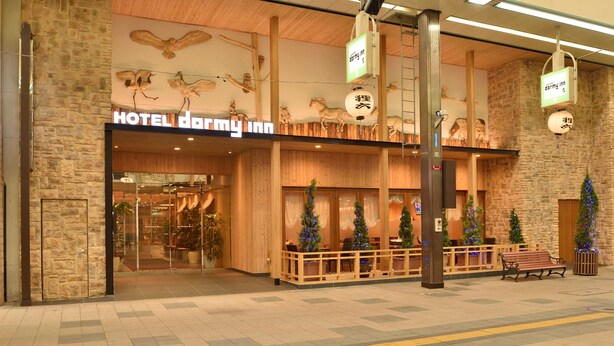 A hotel entrance with a wooden facade, a sign reading "HOTEL Darmy Inn," and Christmas trees. - Dormy Inn PREMIUM Sapporo Hot Spring (Sapporo)
