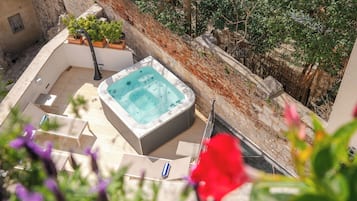 A hot tub in a courtyard with a stone wall and potted plants.