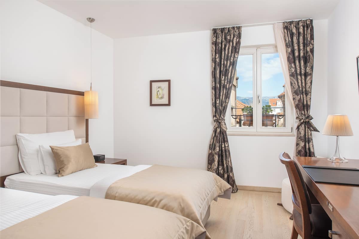 Une chambre d’hôtel avec deux lits, un bureau et une fenêtre avec des rideaux.