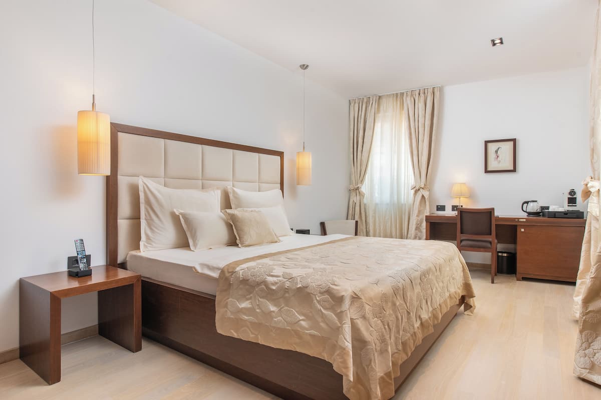 Une chambre d’hôtel avec un grand lit, des tables de chevet, un bureau avec une chaise et une fenêtre avec des rideaux.