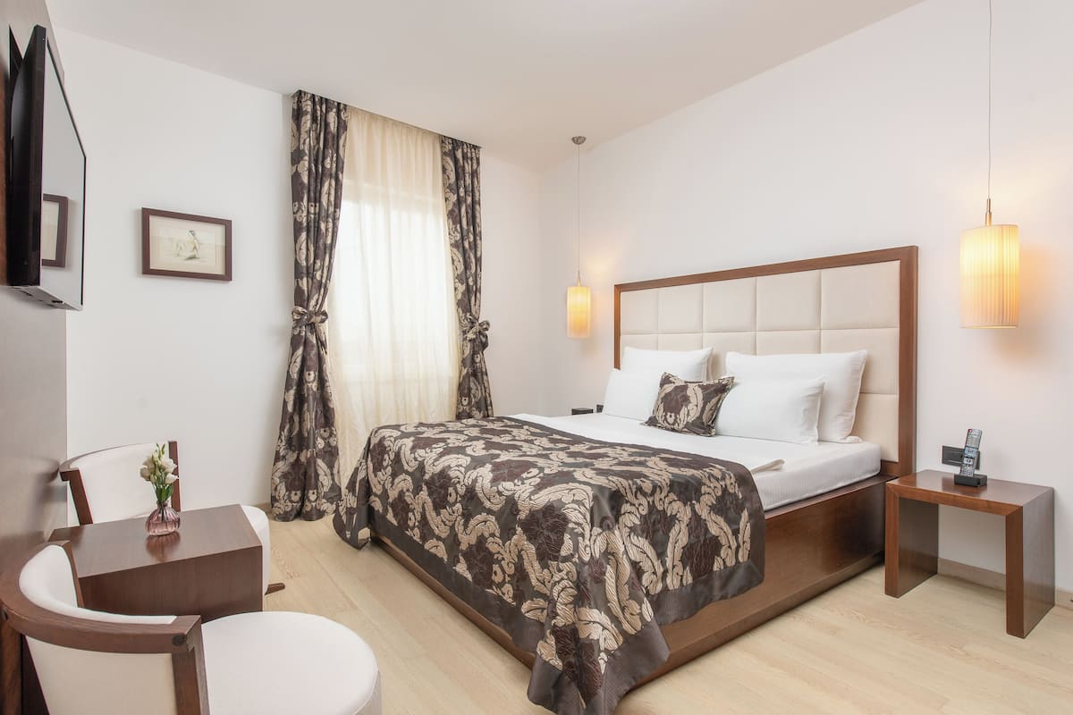 Une chambre d’hôtel avec un grand lit, une table de chevet, une chaise, un bureau et un téléviseur fixé au mur.