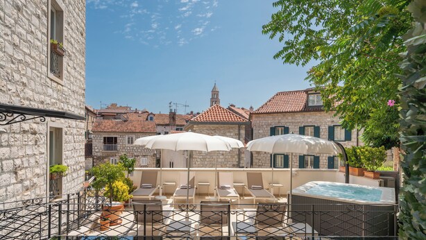 A rooftop pool area with lounge chairs and umbrellas, surrounded by stone buildings with red-tiled roofs and a visible bell tower. - Hotel Marmont Heritage (Split)
