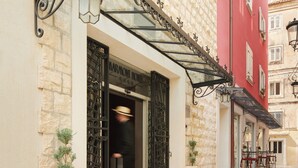 A hotel entrance with a stone facade, a red building adjacent, and a red carpet leading to the door. - Hotel Marmont Heritage (Split)