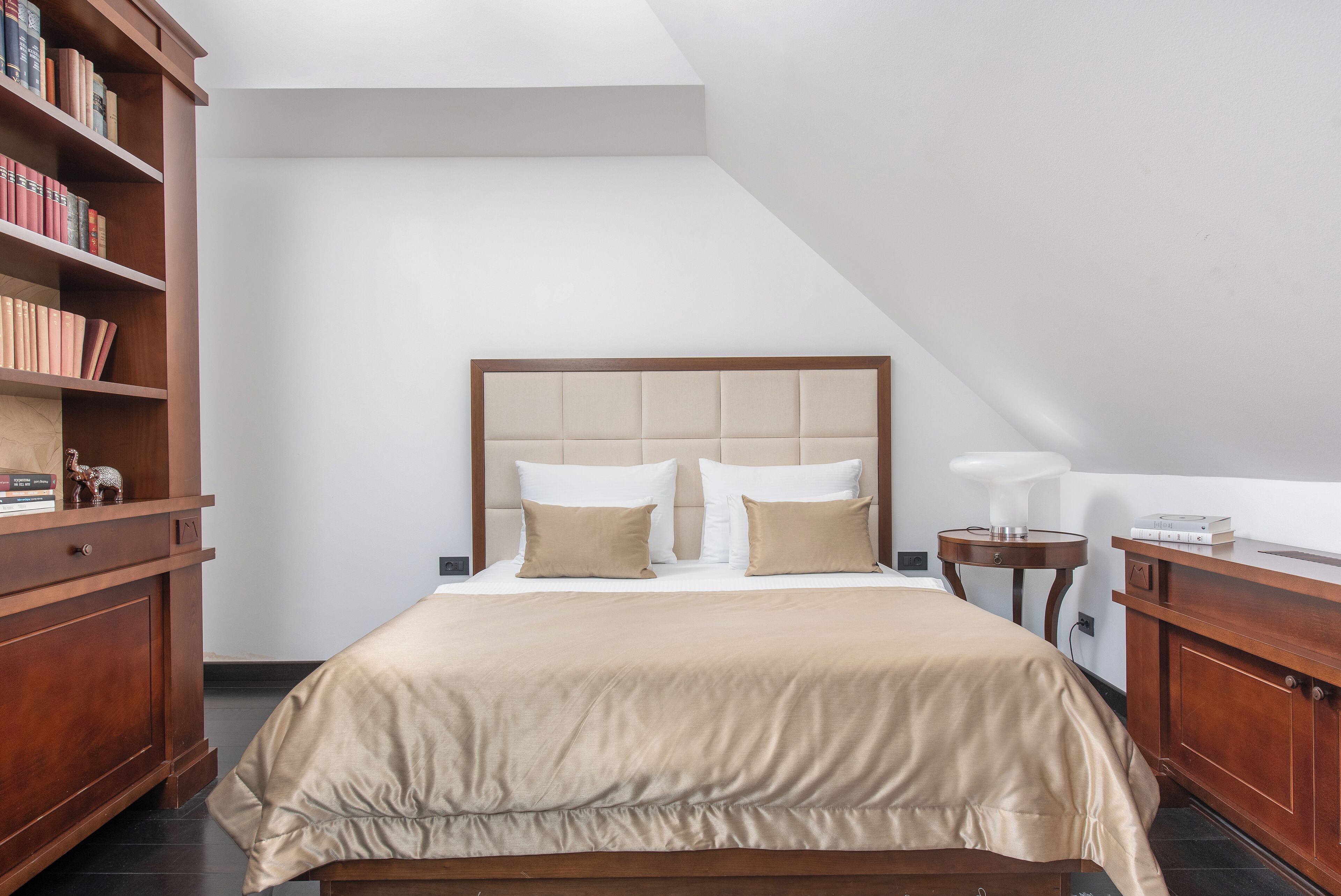 A neatly arranged bedroom with a large bed, a wooden nightstand, a bedside table, and a bookshelf.