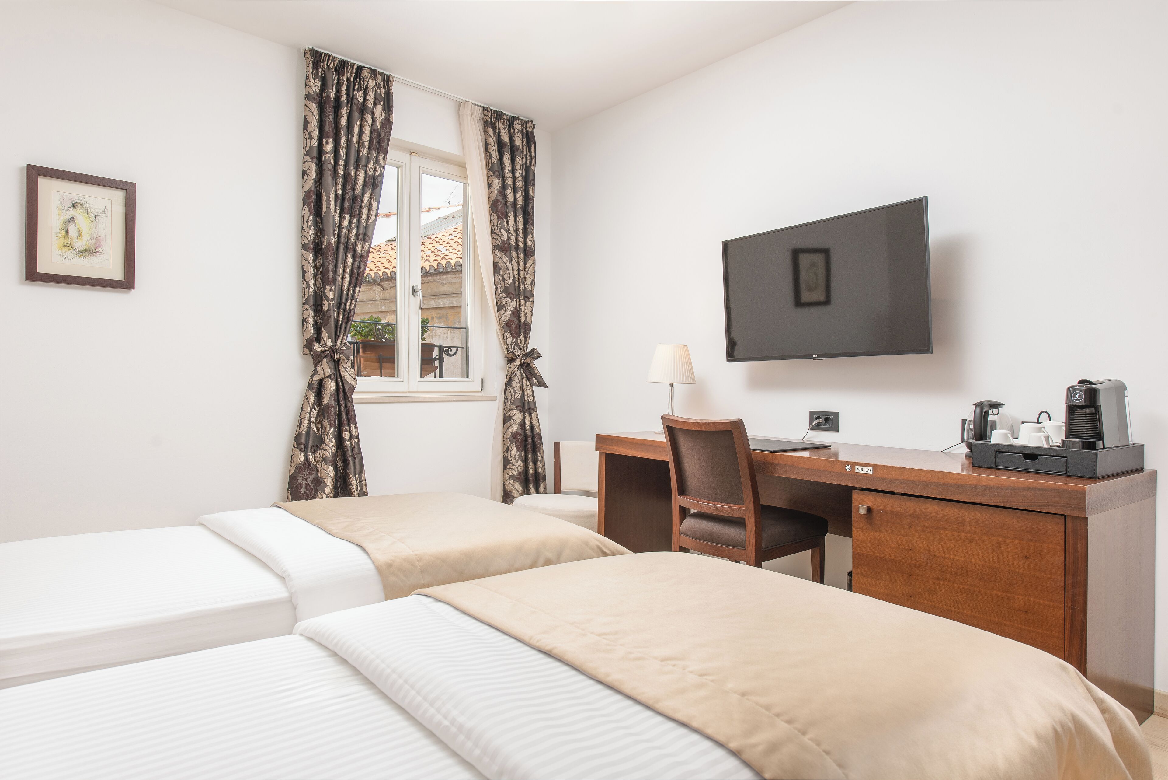 Een hotelkamer met twee eenpersoonsbedden, een bureau met stoel, een televisie en een raam met gordijnen.