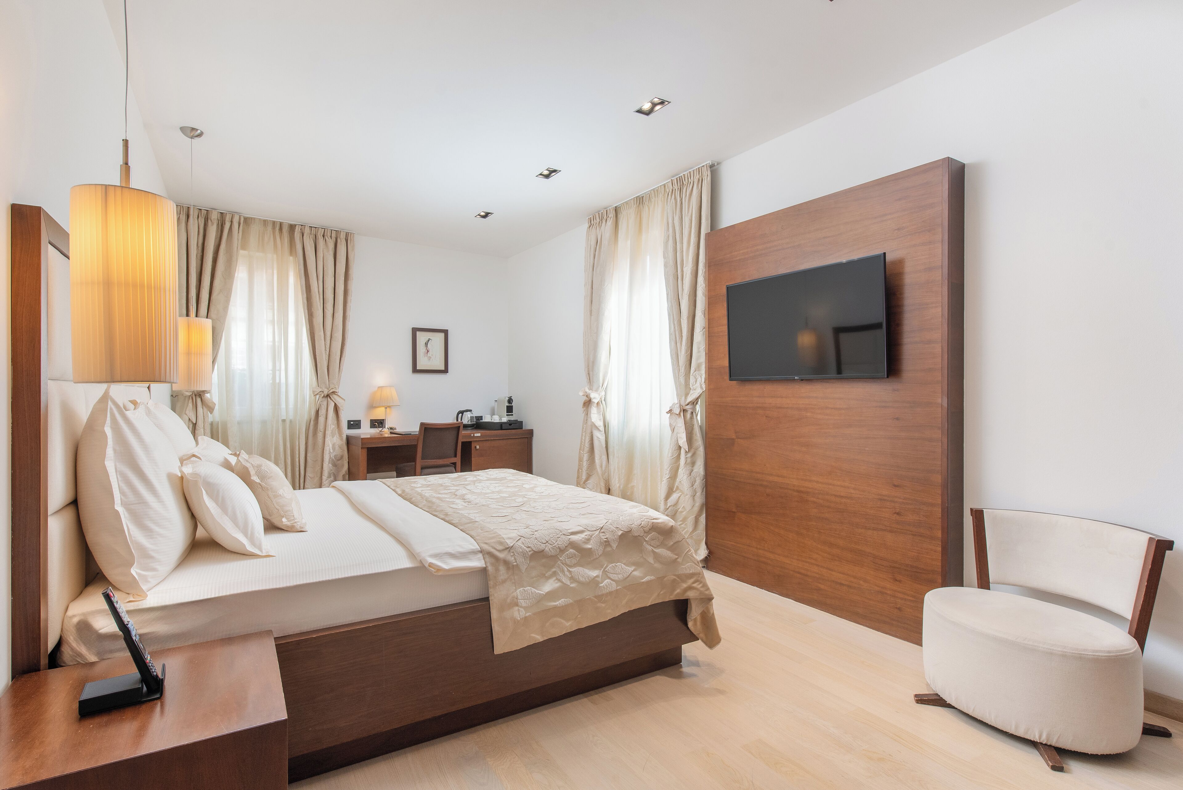 A modern hotel room with a large bed, a desk with a lamp, a TV mounted on the wall, and a chair.
