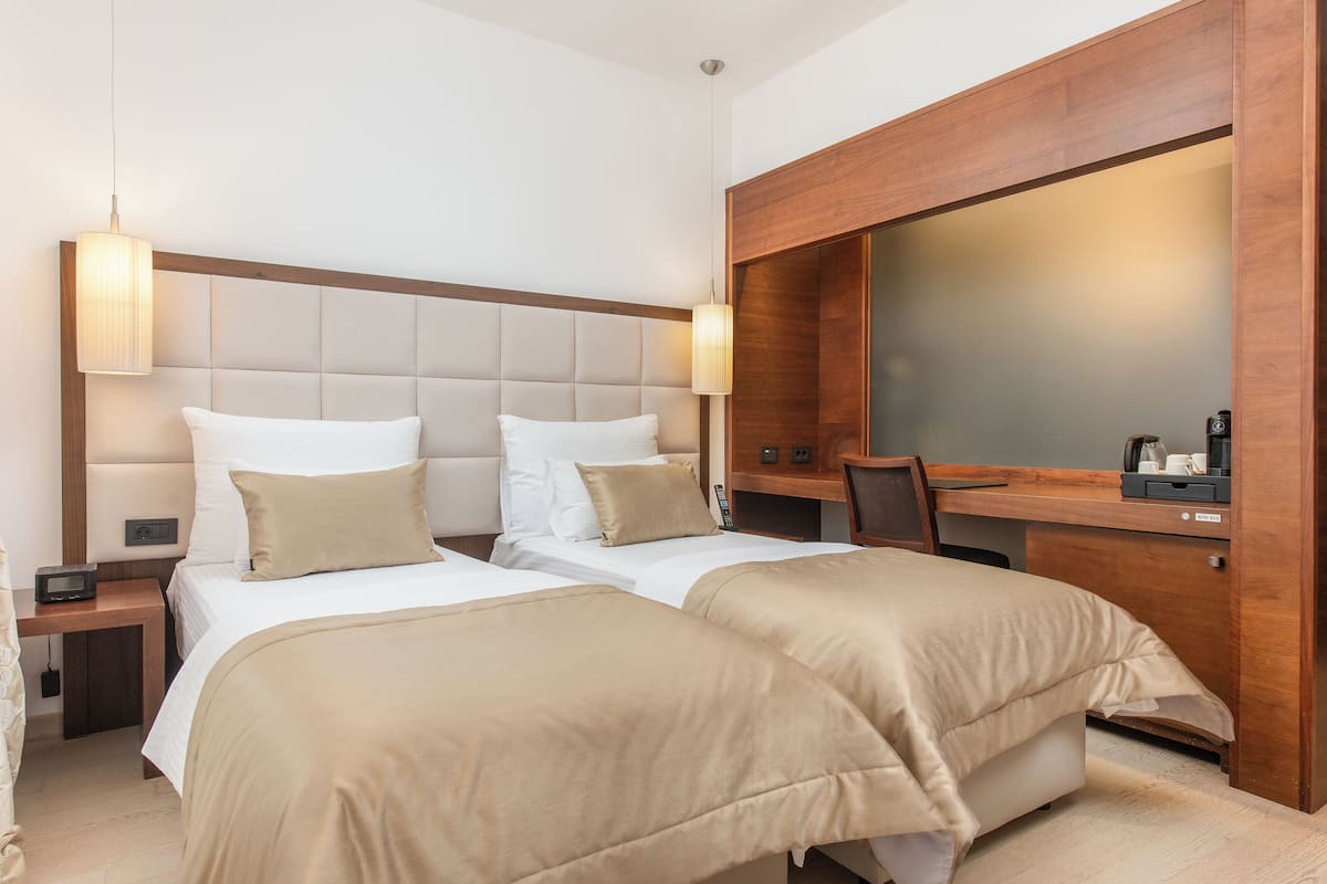 Une chambre d’hôtel avec deux lits, une tête de lit en bois, un grand miroir, un bureau et une chaise.