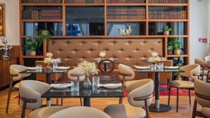 A dining area with tables set for four, a large bookshelf in the background, and a tufted headboard. - Hotel Marmont Heritage (Split)