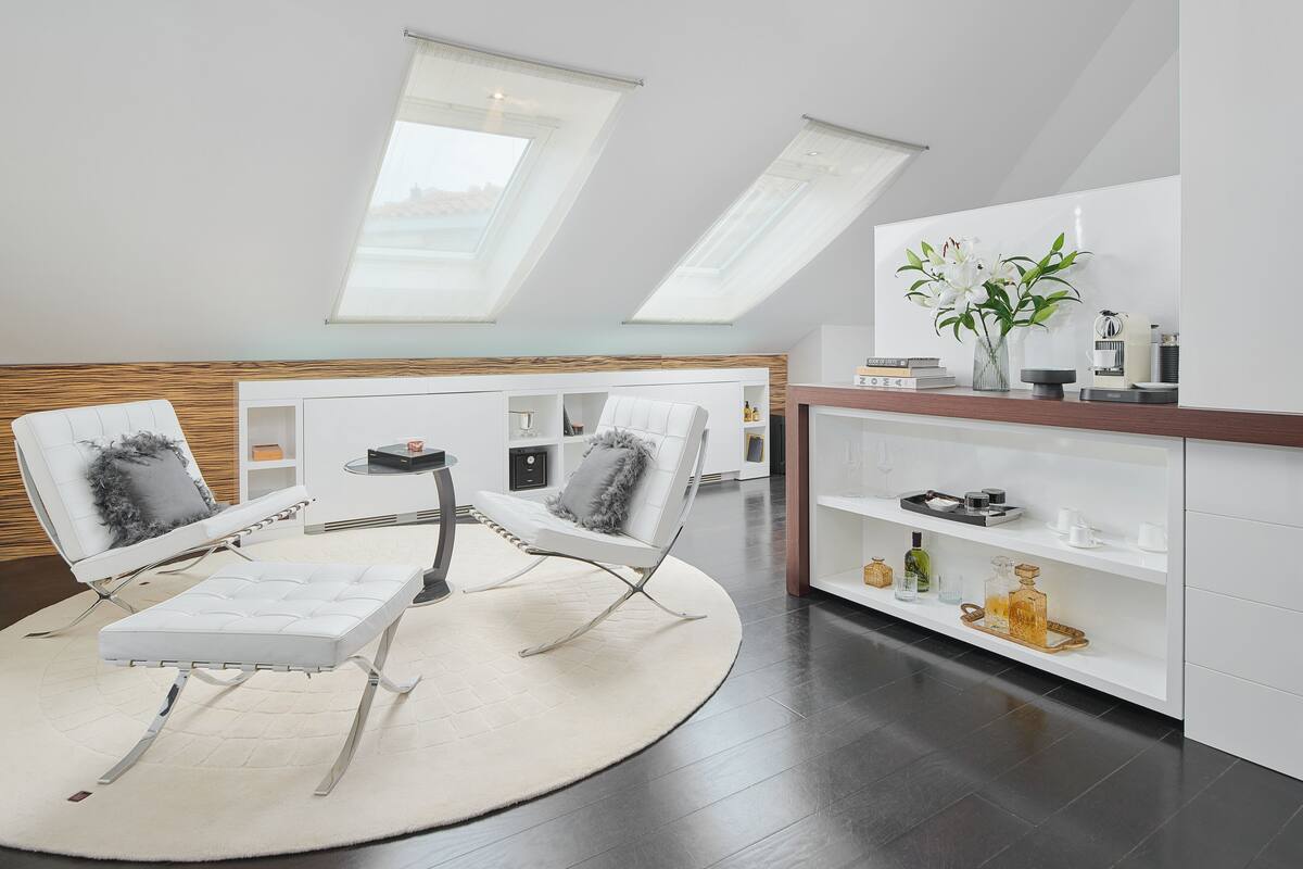 Une chambre de style loft moderne, dotée d’une lucarne, d’un canapé blanc, d’une table basse ronde et d’une étagère blanche agrémentée d’objets décoratifs.
