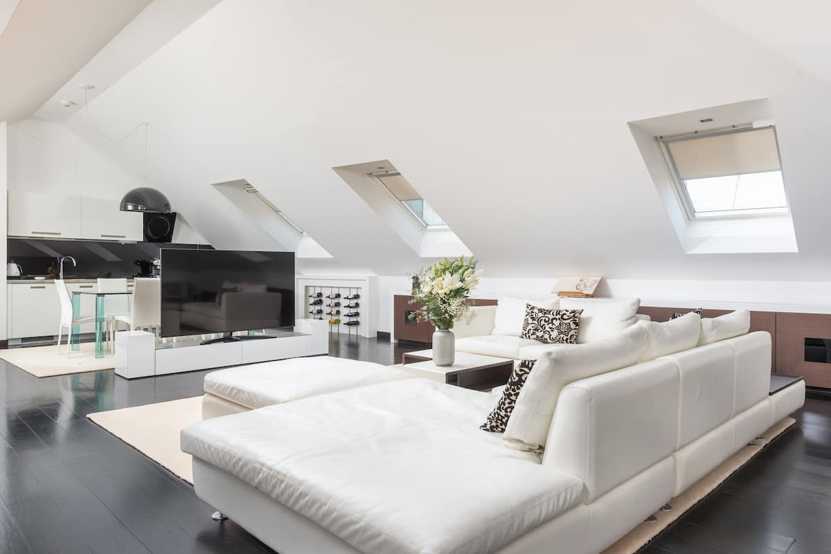 Un salon moderne avec un canapé blanc, un téléviseur à écran plat et un coin cuisine comprenant une table à manger et des chaises.