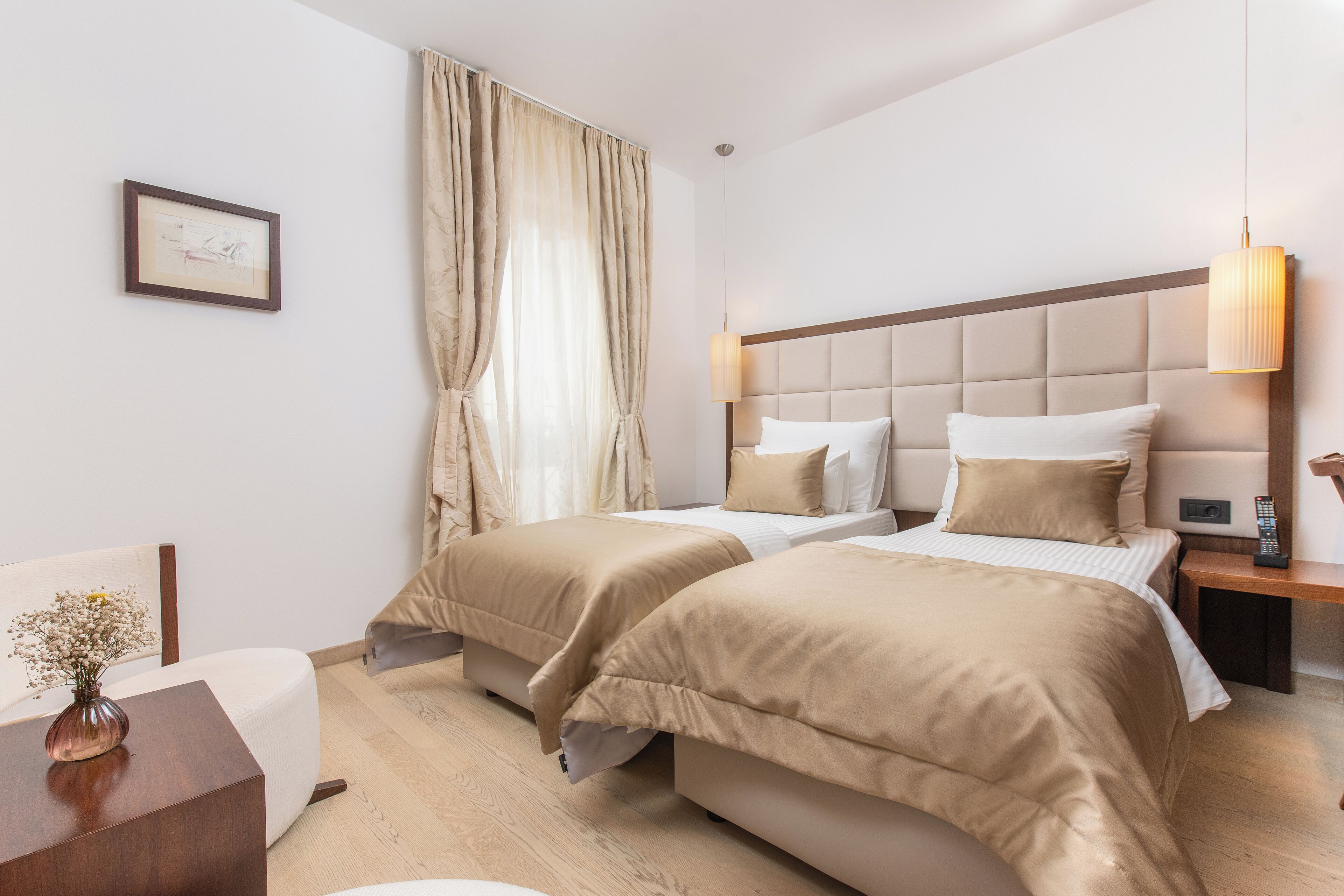 A hotel room with two beds, a bedside table, a lamp, and a framed picture on the wall.