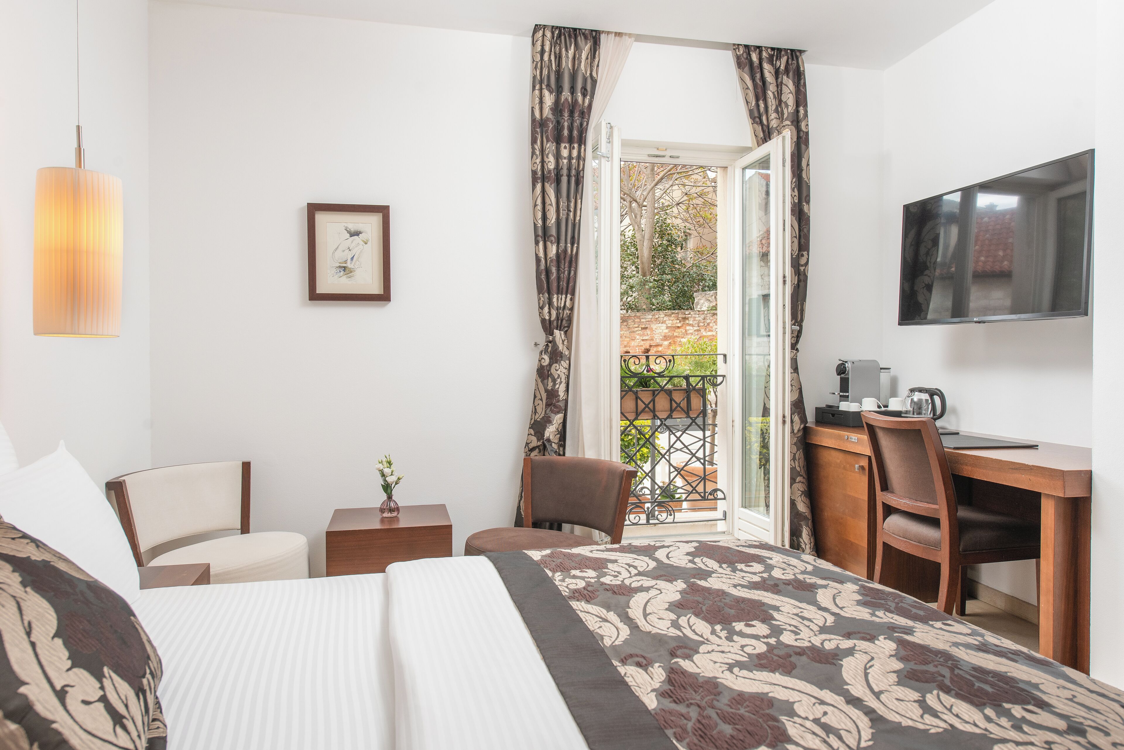 Quarto de hotel com cama, escrivaninha, poltrona, televisão e varanda com vista para o exterior.