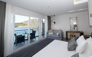 A hotel room with a large bed, a desk, a chair, a sofa, and a balcony with a view of the sea.