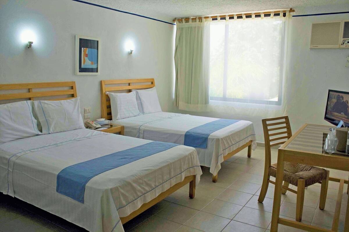 Habitación de hotel con dos camas, un escritorio, una silla, un televisor y una ventana con cortinas.