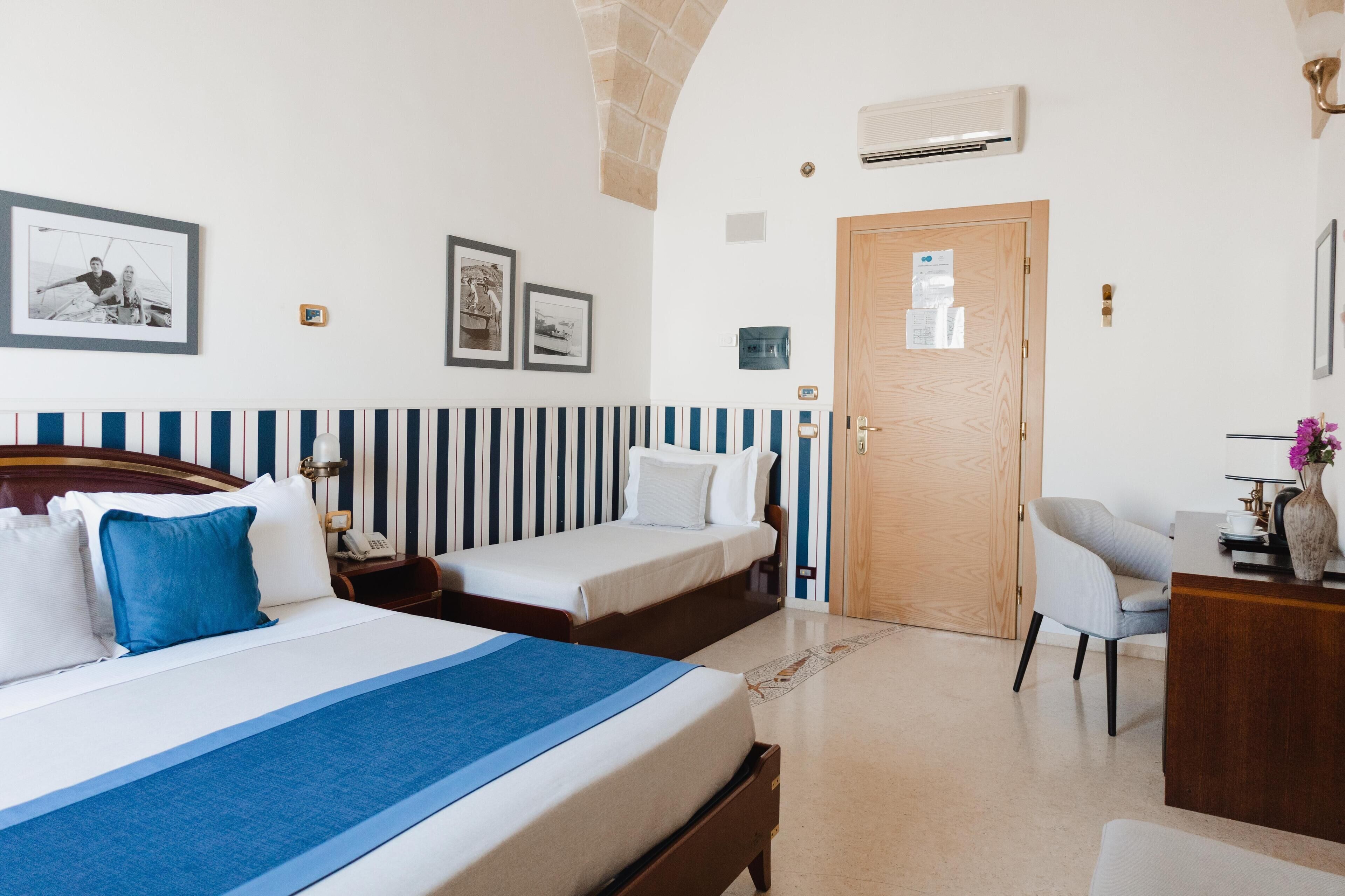 A hotel room with a large bed, two smaller beds, a desk with a chair, and a wooden door.