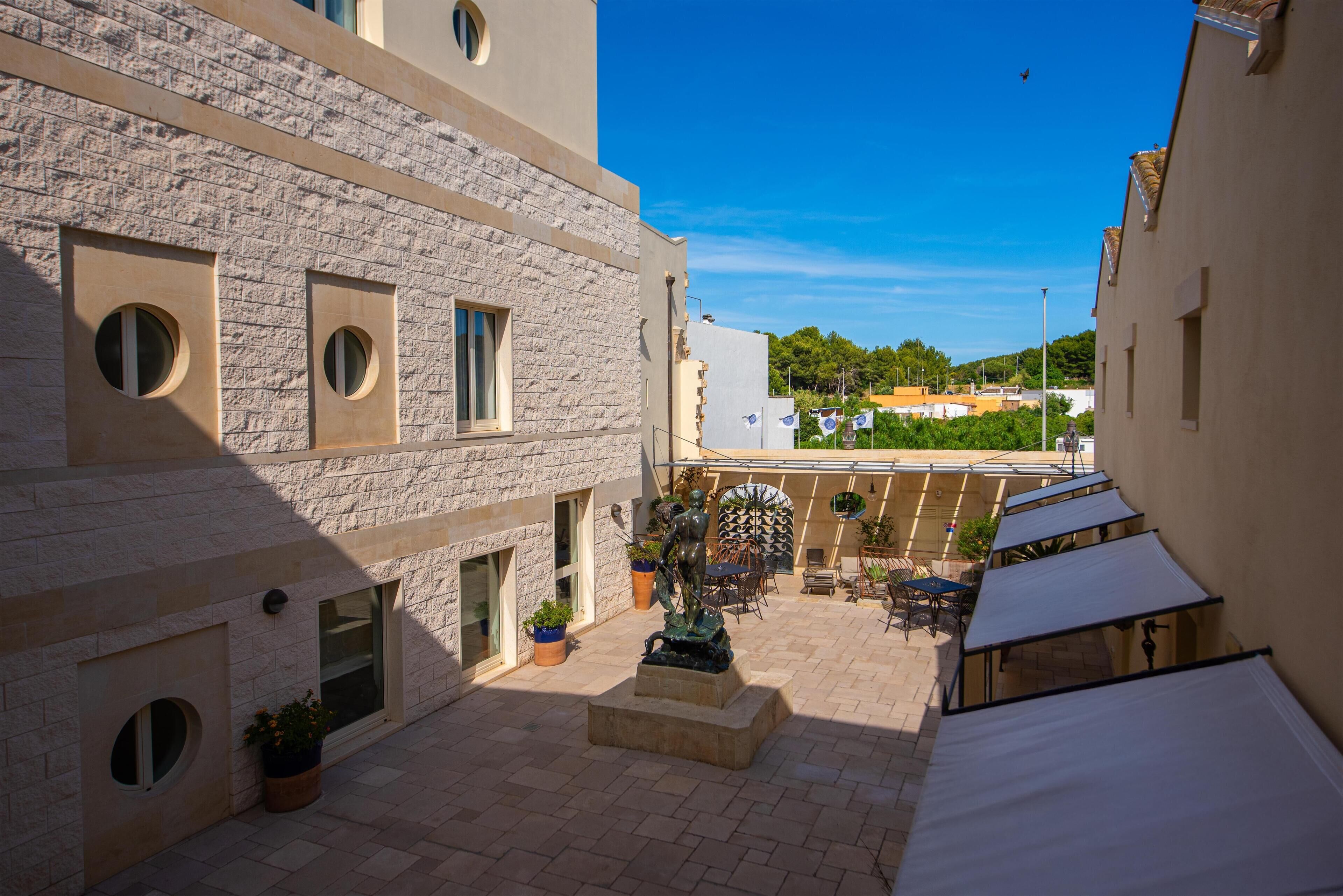 Un cortile con una statua, posti a sedere all'aperto e vista sugli edifici circostanti.