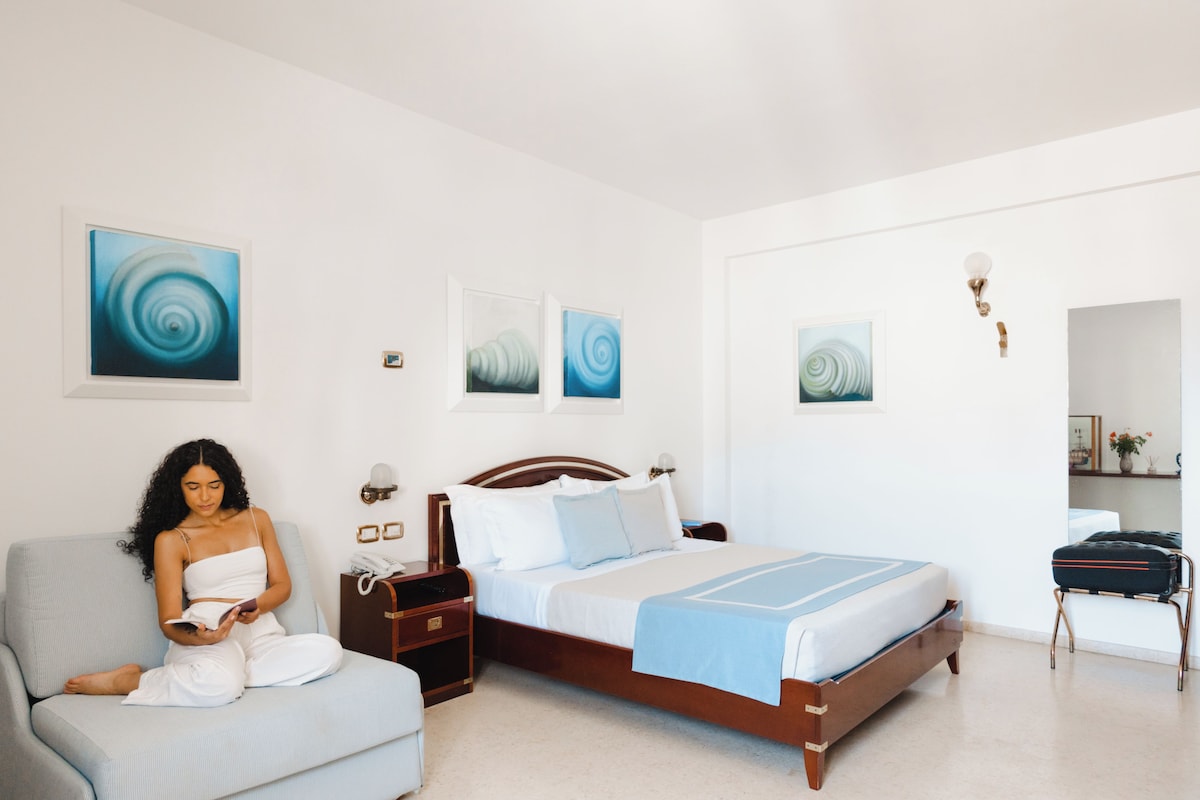Habitació d'hotel amb llit, zona de seients i obres d'art a les parets.