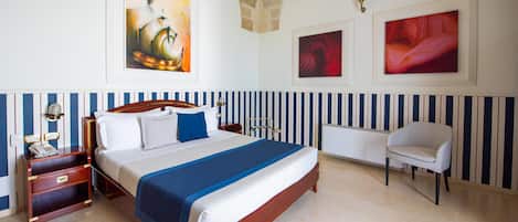 A hotel room with a large bed, a bedside table with a lamp, a chair, and artwork on the walls.
