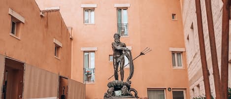 A courtyard with a statue, a building with multiple windows, and a paved walkway.